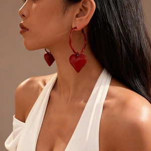 Red heart pendant hoop earrings in geometric style worn by a model in a close-up view