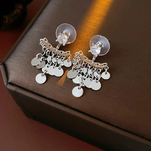 Close-up of silver tassel earrings with round sequins on a brown leather jewelry box