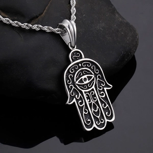 Detailed close-up of a silver Hamsa hand pendant with intricate filigree on a dark rock