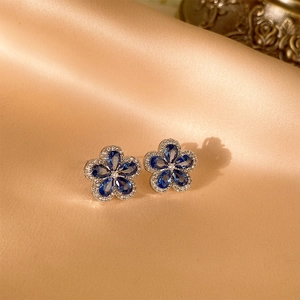 Detailansicht der silbernen Blumenohrringe mit blauen Zirkonia auf Seidenhintergrund