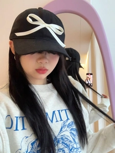 Detail of a black baseball cap featuring a large white 3D bow accent and wide brim