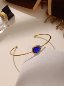 Detailed close-up of a gold teardrop blue gemstone cuff bracelet on white leather
