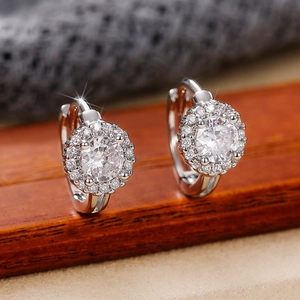 Silver-tone huggie hoop earrings with round-cut zircon halo design on wooden display