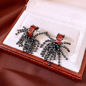 Detail of gothic silver stud earrings with red rectangular stones and black bead tassels