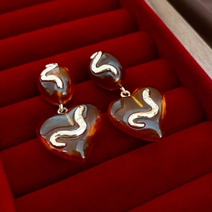 Macro view of amber acrylic heart earrings with gold metal wavy details in a velvet box