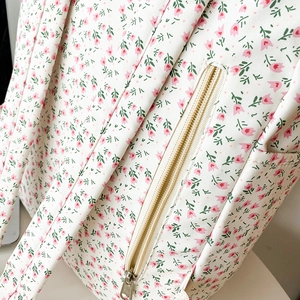 Detailed close-up of pink tulip floral print and metal zipper on white canvas backpack