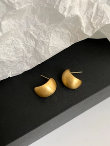 Macro detail of golden matte semi-circular earrings with a brushed metal texture finish