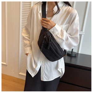 Detail of black canvas chest bag with adjustable strap and embroidery on white shirt