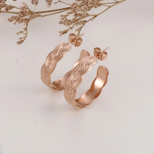 Detail view of rose gold braided texture hoop earrings on a minimalist cream background