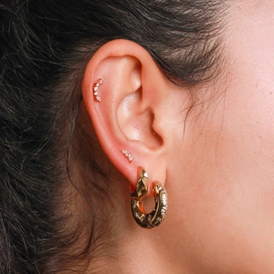Detail of C-shaped gold hoop earrings with star engravings and zircon studs on model ear