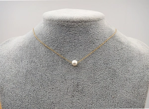 Detail of single white pearl pendant on a fine gold chain displayed on a velvet mannequin