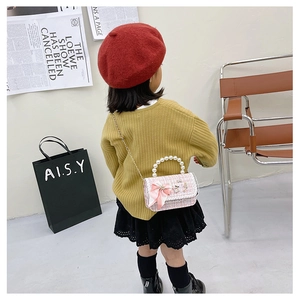 Pink tweed crossbody bag with pearl handle and bow shown on a child model in a shop