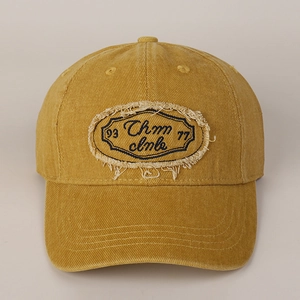 Detail of vintage yellow cotton baseball cap with embroidered letter patch and frayed edges