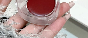 Macro shot of deep red matte lip and cheek mud paste in a heart-shaped clear jar