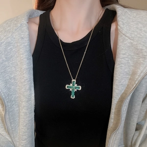 Détail d'un pendentif croix en zircon vert avec chaîne dorée portée sur le cou