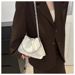 Close-up of a white ruched cloud bag with silver chain strap worn with a brown blazer