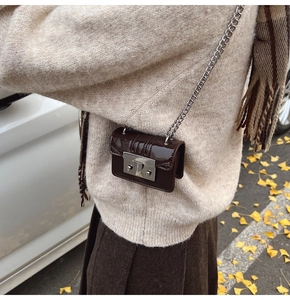 Close-up of a mini brown patent leather chain bag with a metal lock on a model in autumn