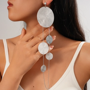 Close-up of long silver tassel earrings with textured round metal discs on a model