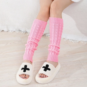 Detail of pink cable knit leg warmers paired with white plush slippers in a cozy home setting