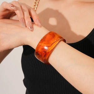 Detail of amber resin bangle showing translucent sand-like texture on model's wrist