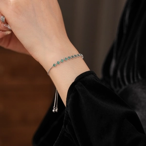 Close-up of sparkling four-leaf clover bracelet with green zircon on woman's wrist