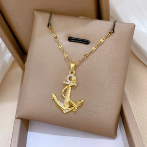 Gros plan d'un collier ancre dorée avec strass micro-pave sur support de boîte à bijoux