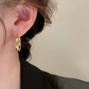 Close-up of a gold C-shaped metal hoop earring worn by a model to show size and luster