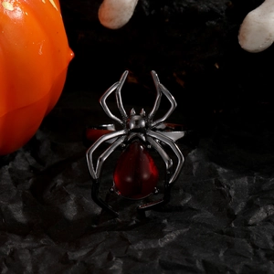 Bague araignée gothique en métal noir avec pierre rouge sur fond décoratif d'Halloween
