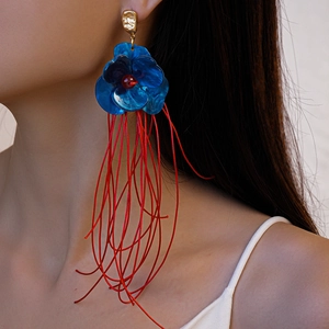 Détail de boucles d'oreilles artistiques avec fleurs en acrylique bleu et franges rouges