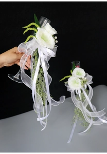 Close-up of elegant white artificial flowers with pearls and long ribbons for wedding glasses
