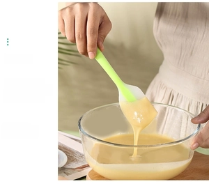 Green silicone spatula scraping batter from a glass bowl during cake baking