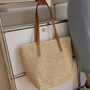 Detail view of woven straw tote bag with brown leather handles and handmade texture