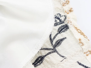 Detail der marineblauen Blattstickerei auf beigem Leinenkleid mit Qualitätsnähten