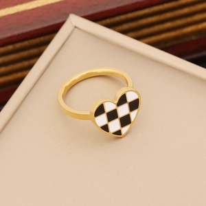 Anello dorato a forma di cuore con motivo a scacchi bianco e nero su supporto beige