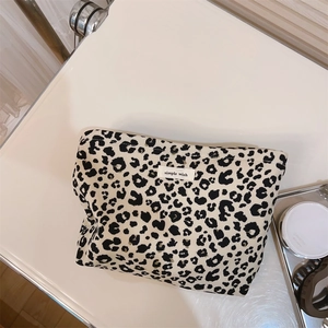 Detailed close-up of leopard print canvas makeup bag with woven brand label on off-white surface