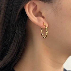 Close-up of golden twist hoop earrings on a model showing a spiral textured design