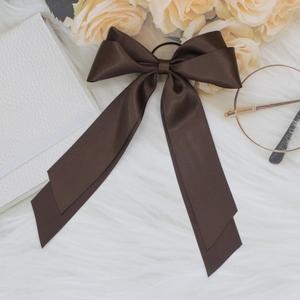 Detail of a dark brown satin bow hair clip with long ribbons on white plush fabric