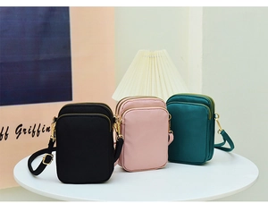 Three-layer nylon crossbody phone bags in black, pink, and dark green on a table