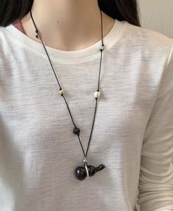 Close-up of black gourd pendant with pearl detail on a woven rope necklace