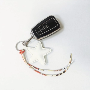 Detail of star-shaped leather bag charm with ribbon and black car key fob cover