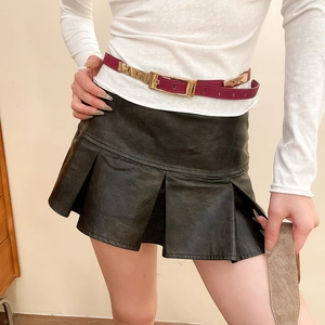 Detail of burgundy slim leather belt with metal buckle on black pleated mini skirt