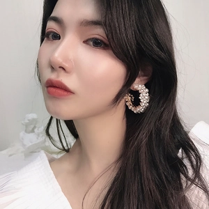 Detail view of large C-shaped pearl hoop earrings worn by a model in a retro style