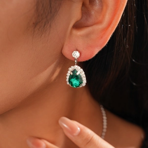 Detailed close-up of emerald green teardrop earring with silver pavé rhinestone border