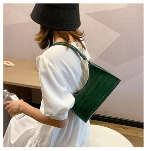 Detail showing green crocodile pattern texture on shoulder bag worn by model