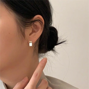 Close-up of minimalist silver rectangular stud earrings worn on ear with polished finish