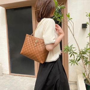 Brown quilted tote bag with golden chain strap and pearl crown charm in outdoor setting