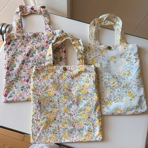 Detailed top view of three floral cotton handbags with metal button closures and handles