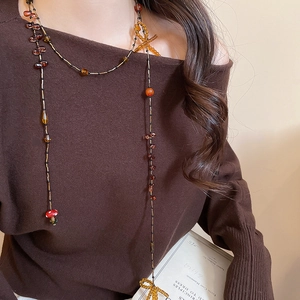 Detail of vintage beaded necklace with red mushroom and yellow bow on model wearing brown knit