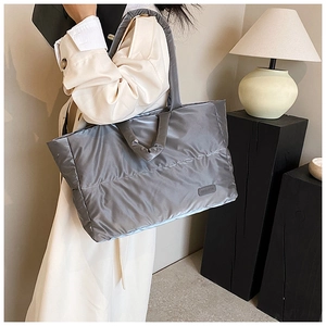 Détail d'un sac cabas matelassé gris en nylon porté par un mannequin en trench-coat