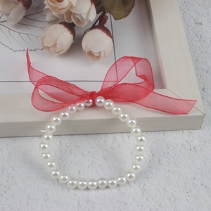 Detailed view of white pearl bracelet featuring a red ribbon bow on a decorative floral background